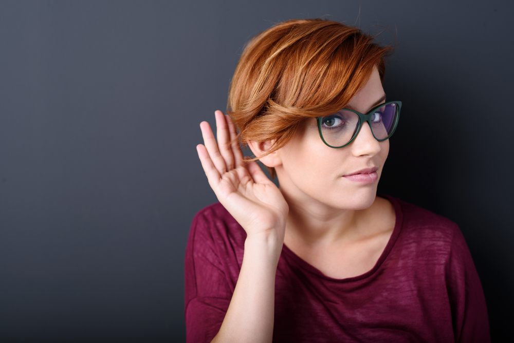 Young woman with a hearing disorder or hearing loss cupping her hand behind her ear with her head turned aside to try and amplify and channel the available sound to her ear drum Young woman with a hearing disorder or hearing loss cupping her hand behind her ear with her head turned aside to try and amplify and channel the available sound to her ear drum